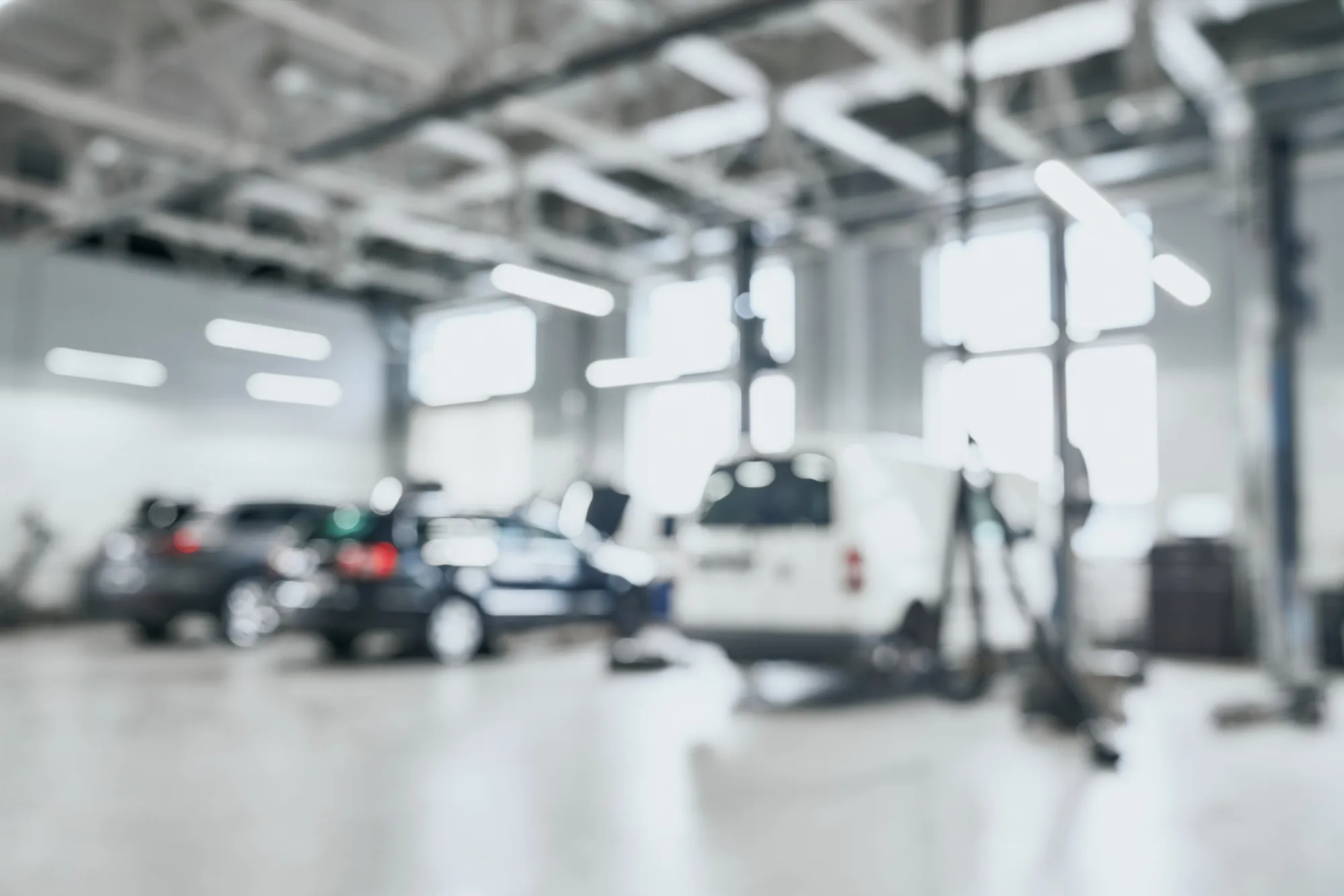 Atelier automobile lumineux avec plusieurs véhicules et ponts élévateurs en arrière-plan flou.