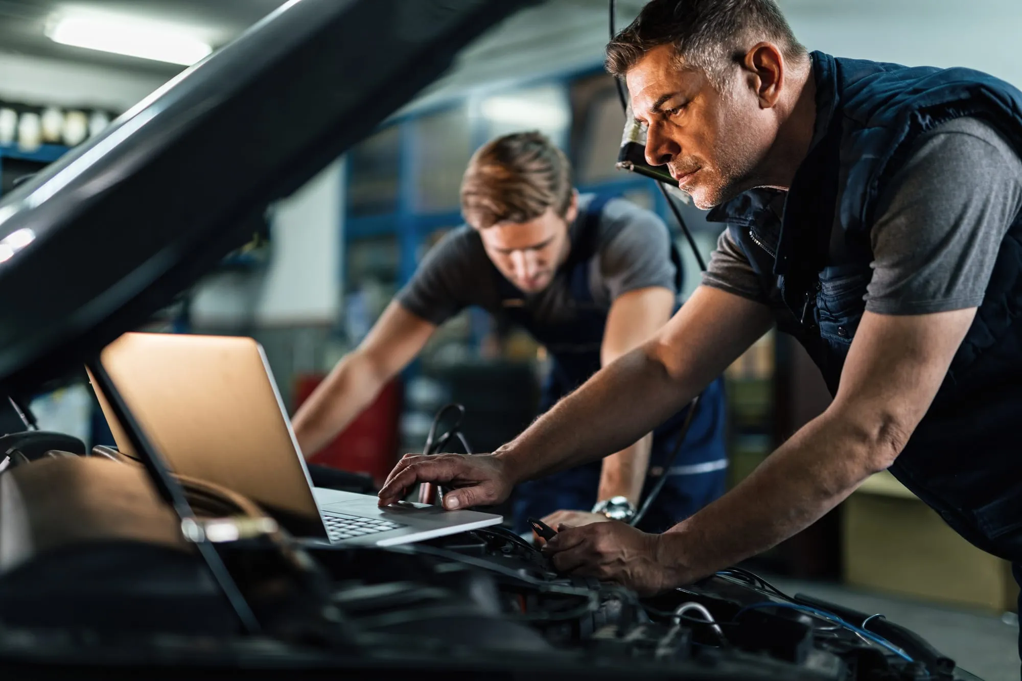 Deux mécaniciens réalisent un diagnostic automobile sous le capot d’un véhicule.