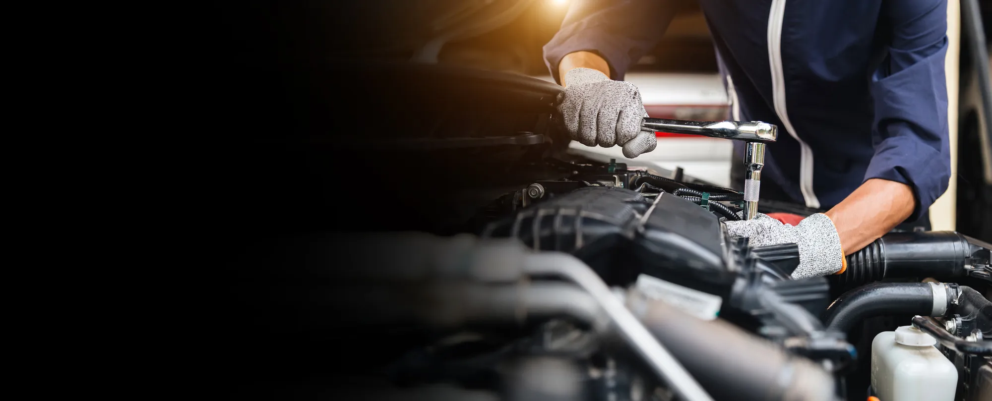 Mécanicien utilisant une clé à cliquet sur un moteur automobile.