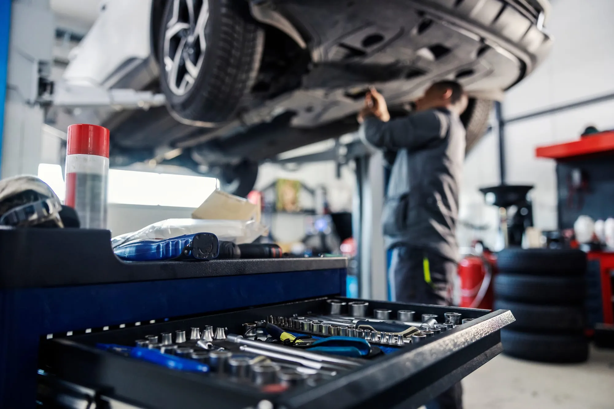 Servante d’outils ouverte devant un mécanicien travaillant sous un véhicule surélevé.