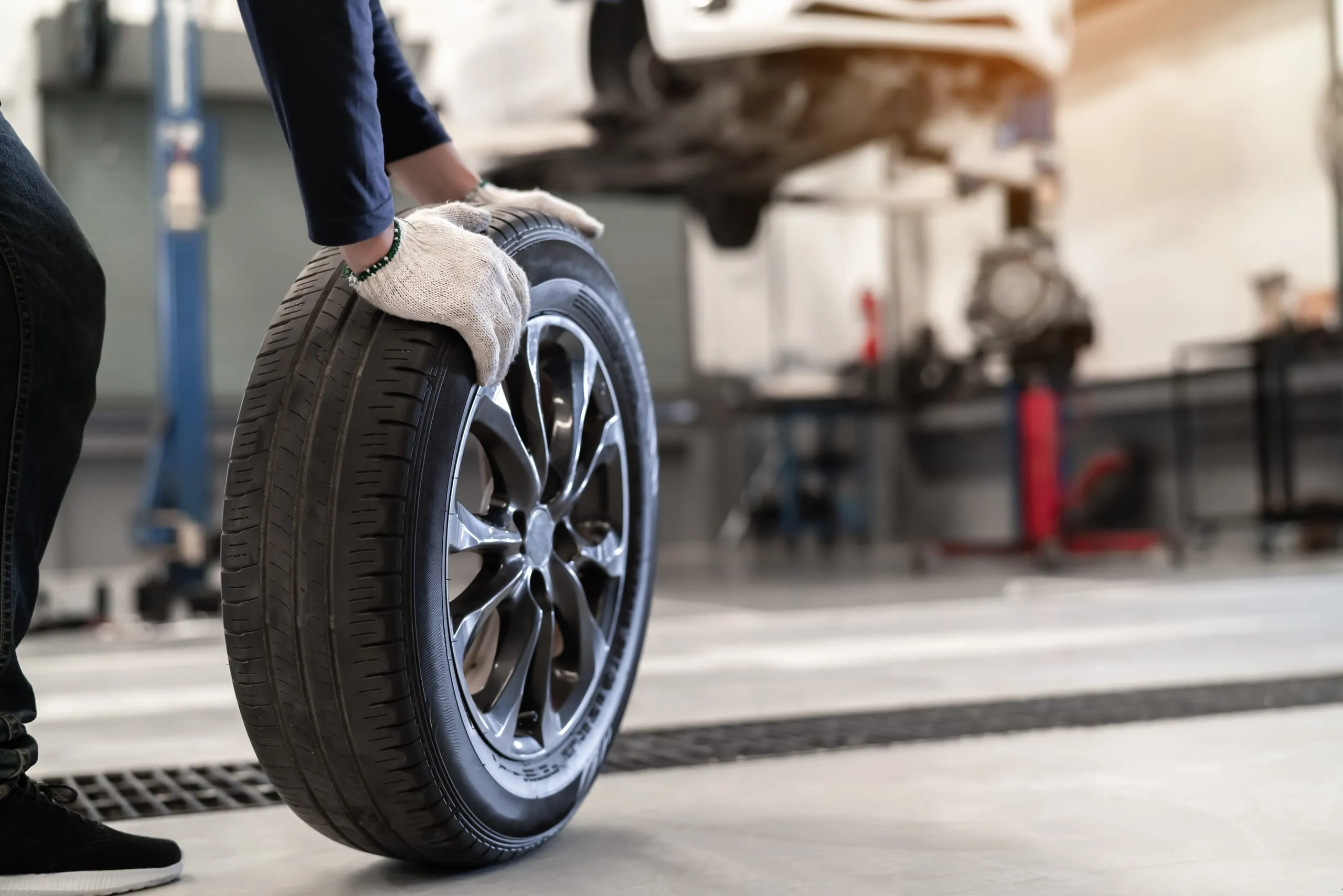 Personne gantée manipulant une roue équipée d’un pneu dans un atelier automobile.
